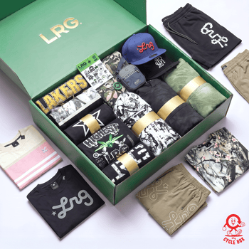 An open green LRG gift box filled with folded apparel, surrounded by matching folded items laid outside the box on a white background. Visible products include black shorts with white LRG logos, black t-shirts with gray LRG logos, camouflage shorts, a blue cap with red LRG lettering, patterned socks, and other coordinated clothing.