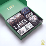 An open green LRG gift box containing multiple LRG-branded items, including a small purple crossbody bag, a patterned wallet or card holder, a black T-shirt with large white LRG lettering, a sticker pack, a patterned notebook or card, and a gray cap, all arranged on a clean white background.