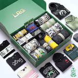 An open green LRG gift box filled with assorted folded apparel and accessories, surrounded by additional clothing items laid out on a white background. Visible brands include LRG on the box and card, Adidas on a black hoodie, and Reebok on a green shirt.